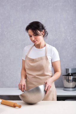 Kadın elinde kaseyle mutfakta yemek pişiriyor. Dikey çerçeve.