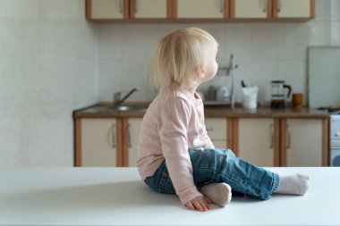 Sevimli sarışın çocuk mutfak arka planında masada oturuyor. Kahvaltı bekliyor..