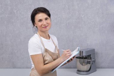 Elinde belgelerle mutfak önlüğü giymiş bir kadın portresi. Aşçı reçete yazıyor..