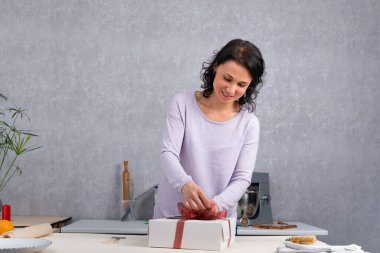 Gülümseyen kadın kırmızı kurdeleli beyaz karton bir kutuda hediye paketliyor. Tatil için hazırlanıyorum..