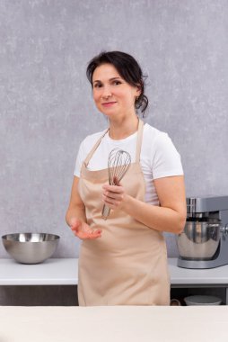 Kadın mutfak önlüğüyle aşçı ve elinde çırpıcıyla. Dikey çerçeve.