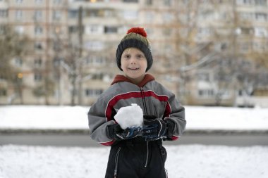 Kış tulumlu çocuk kartopu oynar. Kışın açık havada çocuk portresi.