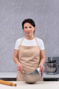 Kadın mutfakta yemek pişiriyor ve elinde metal bir kase tutuyor. Dikey çerçeve.