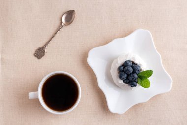 Düz konmuş kahvaltı. Bir fincan kahve, çilekli kek ve kaşık. Üst görünüm.