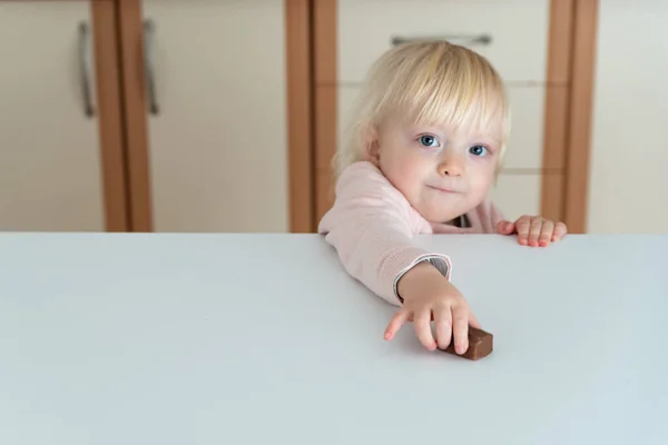 Kleines Blondes Mädchen Greift Nach Schokoladenbonbons Die Auf Dem Tisch — Stockfoto