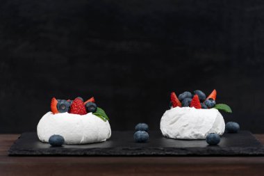Siyah arka planda Anna Pavlova pastası. Taze çilek ve yaban mersinli hava kremalı pasta..