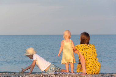 Kumsalda oturan iki çocuklu bir anne. Arkadan bak. Çocuklarla yaz tatili