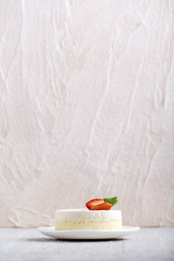 Dikey çerçeve. Çilekli cheesecake beyaz tabakta, arka planda. Yan görünüm.