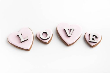 Kalp şeklinde zencefilli kurabiye, beyaz arka planda pembe şekerli krema ve yazıtlı aşk.