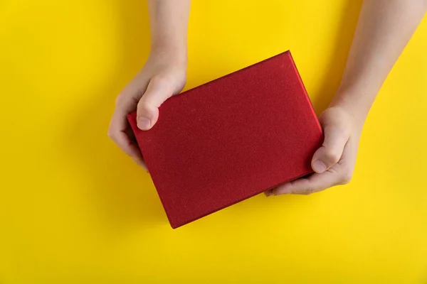 Ręce Dzieci Trzymają Czerwone Kartonowe Pudełko Żółtym Tle Widok Góry — Zdjęcie stockowe