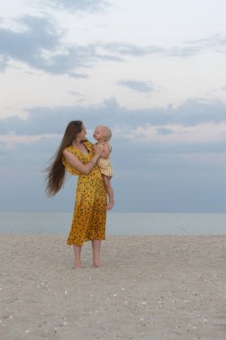 Anne bebeğini deniz kenarında tutuyor. Dikey çerçeve