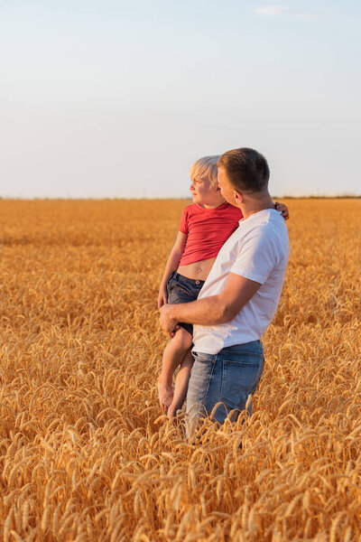 Father and son stand in middle of wheat field. Vertical frame.