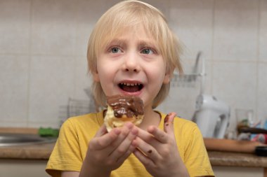 Sarışın çocuk çikolatalı pasta yiyor. Çocuk ekler yer. Zararlı tatlılar.