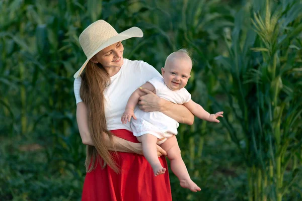 Beautiful young mother holds smiling baby on greenery background. Happy motherhood. Family holidays.