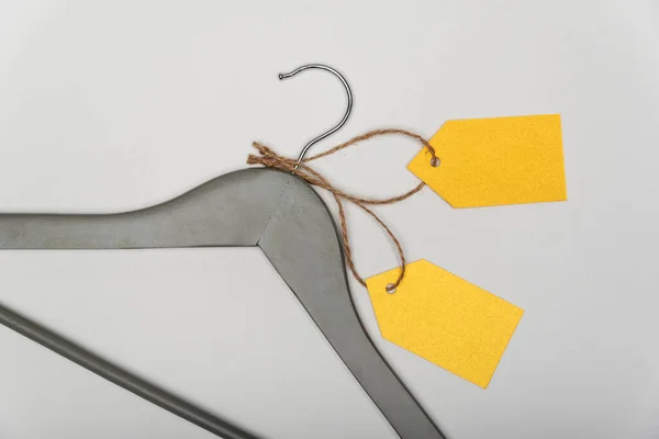 Grey coat hanger with yellow paper labels on white background. Blank label , mockup template. Clothing tag.