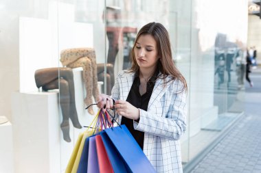 Alışveriş merkezinde çok renkli alışveriş torbaları olan genç bir kadın. Pencere dosyası arkaplanı.