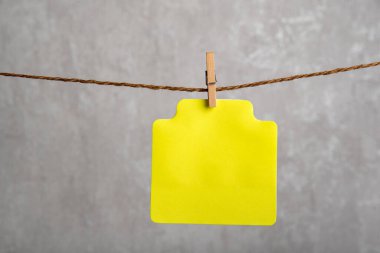 Gri arka planda çamaşır iğnesiyle asılı boş sarı kağıt kart. Uzayı kopyala Metnin için yer