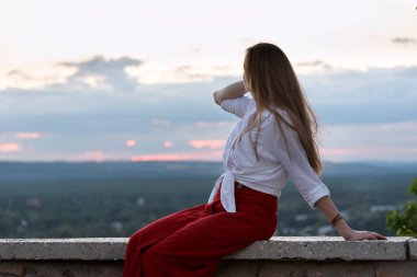 Yan görüş panoramik platformunda genç ve güzel bir kadın. Gün batımı ve orman uzakta..