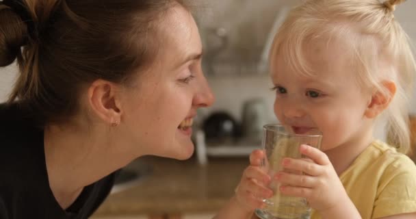 Маленькая блондинка на кухне пьет воду из стакана и делится с матерью. — стоковое видео