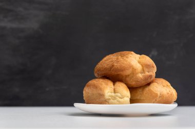 Beyaz tabakta üç iştah açıcı profiterol. Ev yapımı yumurtalar ve ekinler. Kremasız ekler..