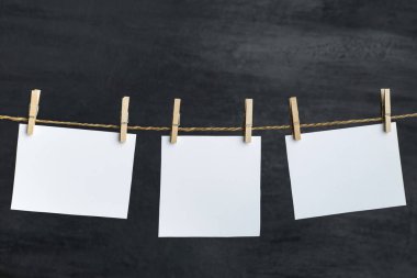 Beyaz boş kağıt notlar ipe asılmış mandallarla. Siyah arka plan. Uzayı kopyala Metnin için yer.