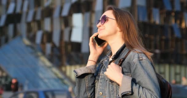 Joyeux jeune femme en lunettes de soleil parlant au téléphone. Touriste dans la ville moderne ensoleillée — Video