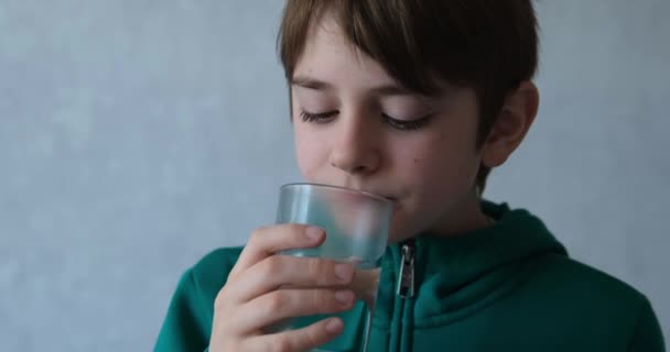 Roztomilý teenager pije vodu ze sklenice. Chlapec spláchne léky. Hnědooký školák pije vodu — Stock video