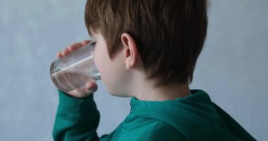 Boy is happy to drink water from a glass. Happy child quenches thirst. Teenager with a glass of water