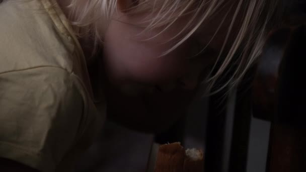 Child hid on the table and eats bread. Hungry child has pulled off a bun and is hiding. Prohibited food — Vídeo de Stock