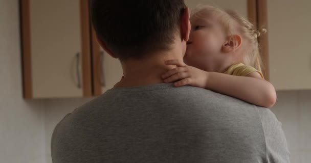 Little blond girl gently hugs her dad. Baby in his fathers arms whispers something to him. Child hugs daddy — Stockvideo