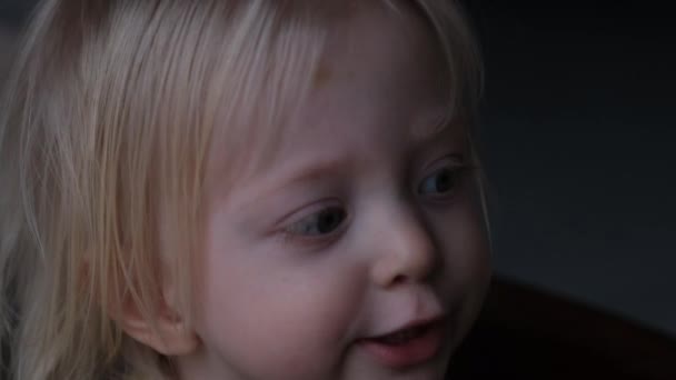 Petit bébé blond lève les yeux et dit quelque chose. Enfant bavard. Portrait d'une petite fille en mode discret. — Video