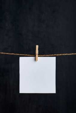İpte mandallarla asılı beyaz boş notlar. Siyah arka plan. Uzayı kopyala Mesajın için yer aç. Dikey çerçeve.