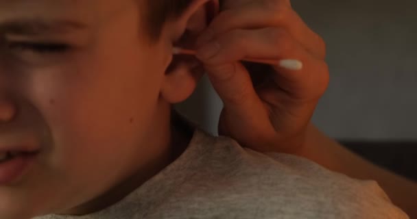 A mão das mulheres limpa a orelha dos rapazes com uma espátula. Close-up. Iluminação natural Falar devagar. — Vídeo de Stock