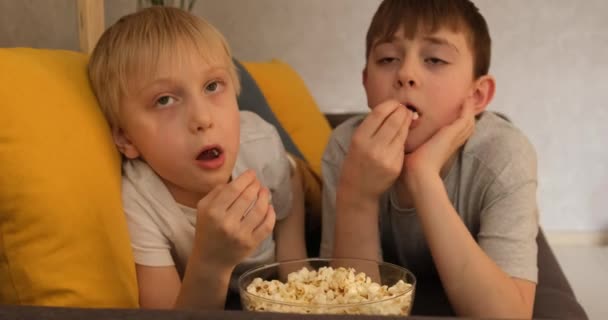 Два маленьких мальчика едят попкорн лежа на диване и смотрят телевизор. крупным планом. daylight — стоковое видео