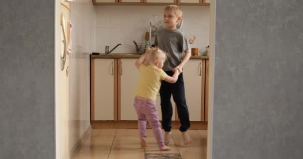 Hermano y hermana saltan felices en la cocina. Los niños saltan y bailan en el apartamento. Dos niños en edad preescolar divirtiéndose en casa — Vídeos de Stock