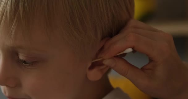 Το χέρι μιας γυναίκας καθαρίζει το αυτί ενός μικρού ξανθού αγοριού. Παιδική υγιεινή. Κοντινό πλάνο. Φυσικό φως ημέρας — Αρχείο Βίντεο