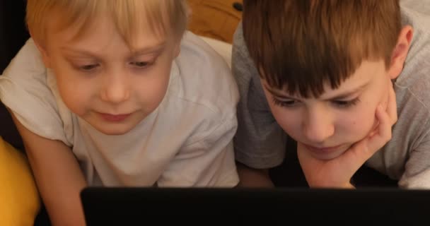 Dos chicos se acuestan en el sofá y juegan en un portátil. Vista frontal. De cerca. — Vídeos de Stock