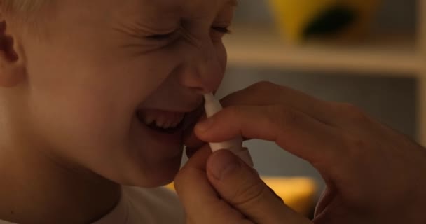 Mão das mulheres injeta um spray nasal para um menino loiro. Procedimentos de higiene em casa. Luz natural. Close-up — Vídeo de Stock