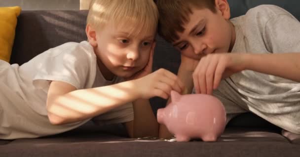 Két kisfiú érméket tett egy malacperselybe. Családi megtakarítás. Nappali elölnézet — Stock videók