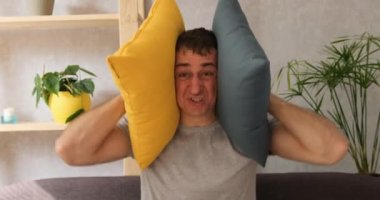 Yorgun ve sinirli genç adam yastıkları örtüyor. Kulakları bağırıyor ve gürültü yapmayı kesmesini istiyor. Portre, gün ışığını kapat