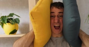 Yorgun ve sinirli genç adam yastıkları örtüyor. Kulakları bağırıyor ve gürültü yapmayı kesmesini istiyor. Portre, gün ışığını kapat