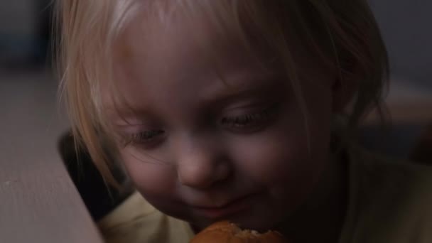 Klein meisje kauwt droevig op een broodje. Close-up portret. Kind eet brood aan tafel. Zelfgemaakt bakken — Stockvideo