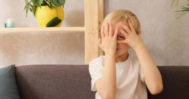 Küçük mutlu sarışın çocuk parmaklarını kapar ve koltukta oturan kameraya el sallar. Gün ışığı