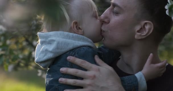O jovem pai tem a filha nos braços. Rapariga abraça e beija o pai. Close-up. Luz do dia. — Vídeo de Stock
