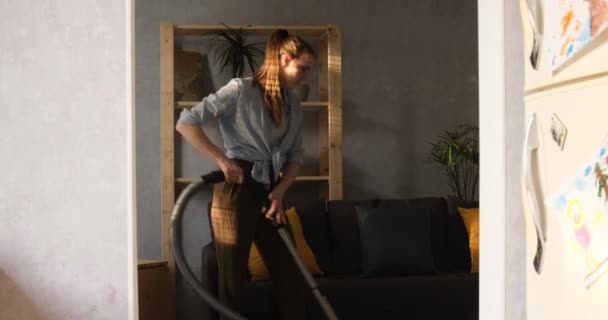 Girl vacuums the room. Young woman cleans apartment. Housewife cleans up at home. Daylight. — Stock Video