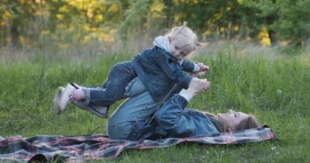 Mother and little girl are playing during picnic in park. Girl flies on mom feet. — Stock Video