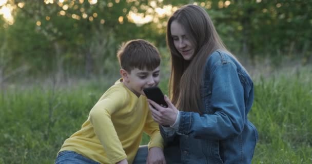 Jonge moeder laat foto per telefoon zien aan haar zoon. Moeder en zoon in park bij picknick. — Stockvideo