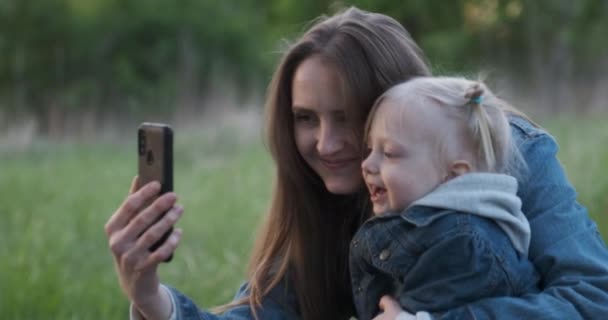 La joven madre se toma selfie con su hija pequeña. Mamá con el niño en el parque tomando fotos de sí mismos — Vídeos de Stock