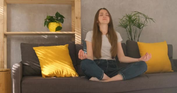 Молода жінка сидить вдома на дивані в положенні лотоса і роздумує . — стокове відео
