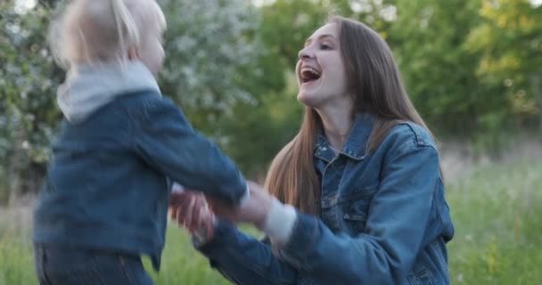 La joven madre juega con su hija pequeña. El niño salta y ríe alegremente, sosteniendo las manos de las mamás. — Vídeos de Stock